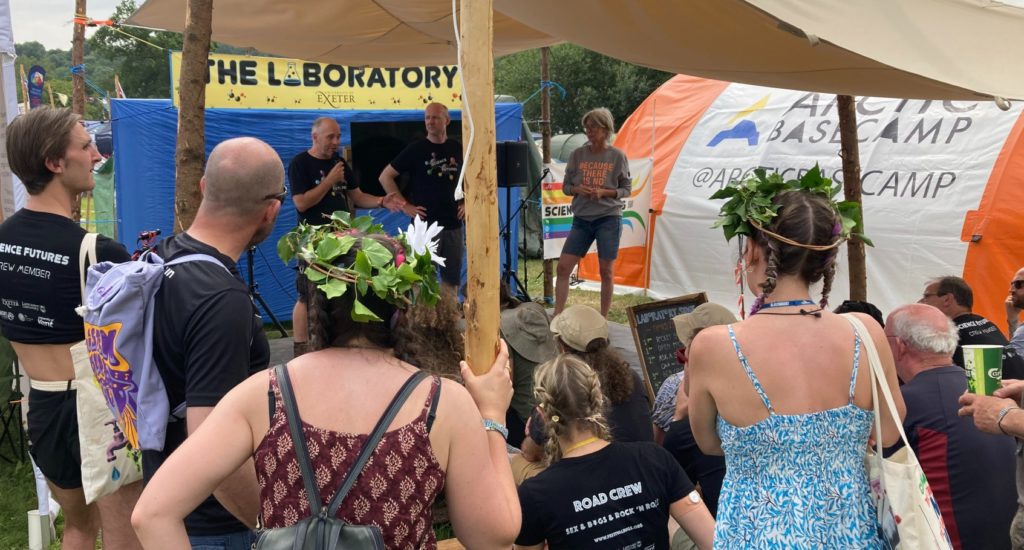 A group of people watching speakers on a stage at Glastonbury