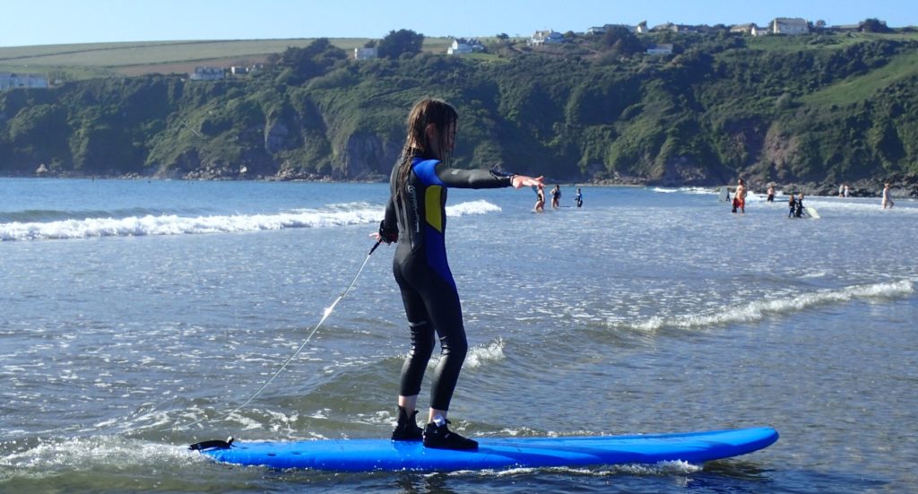 A child standing on a surf board in shallow water on a beach