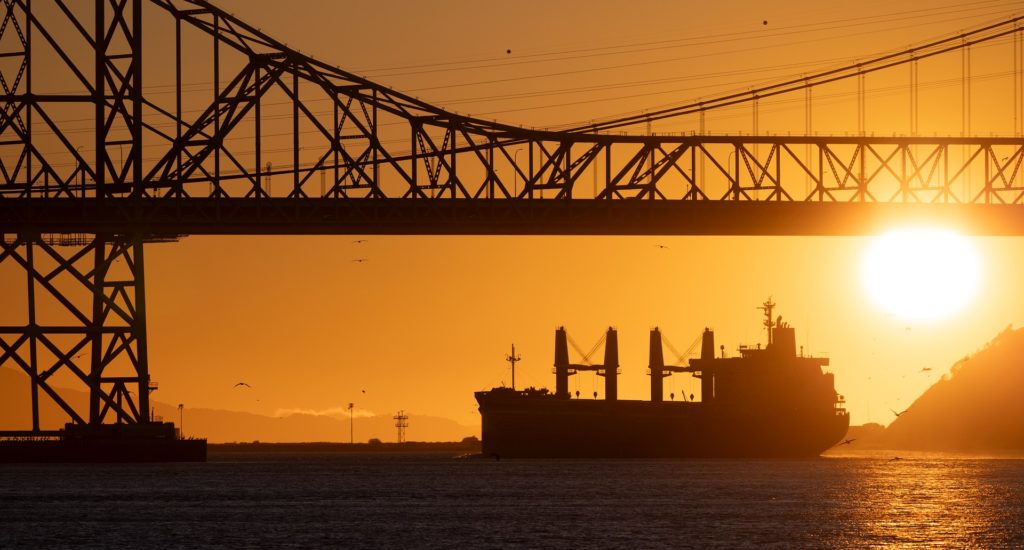 A large tanker ship under a bridge at sunset