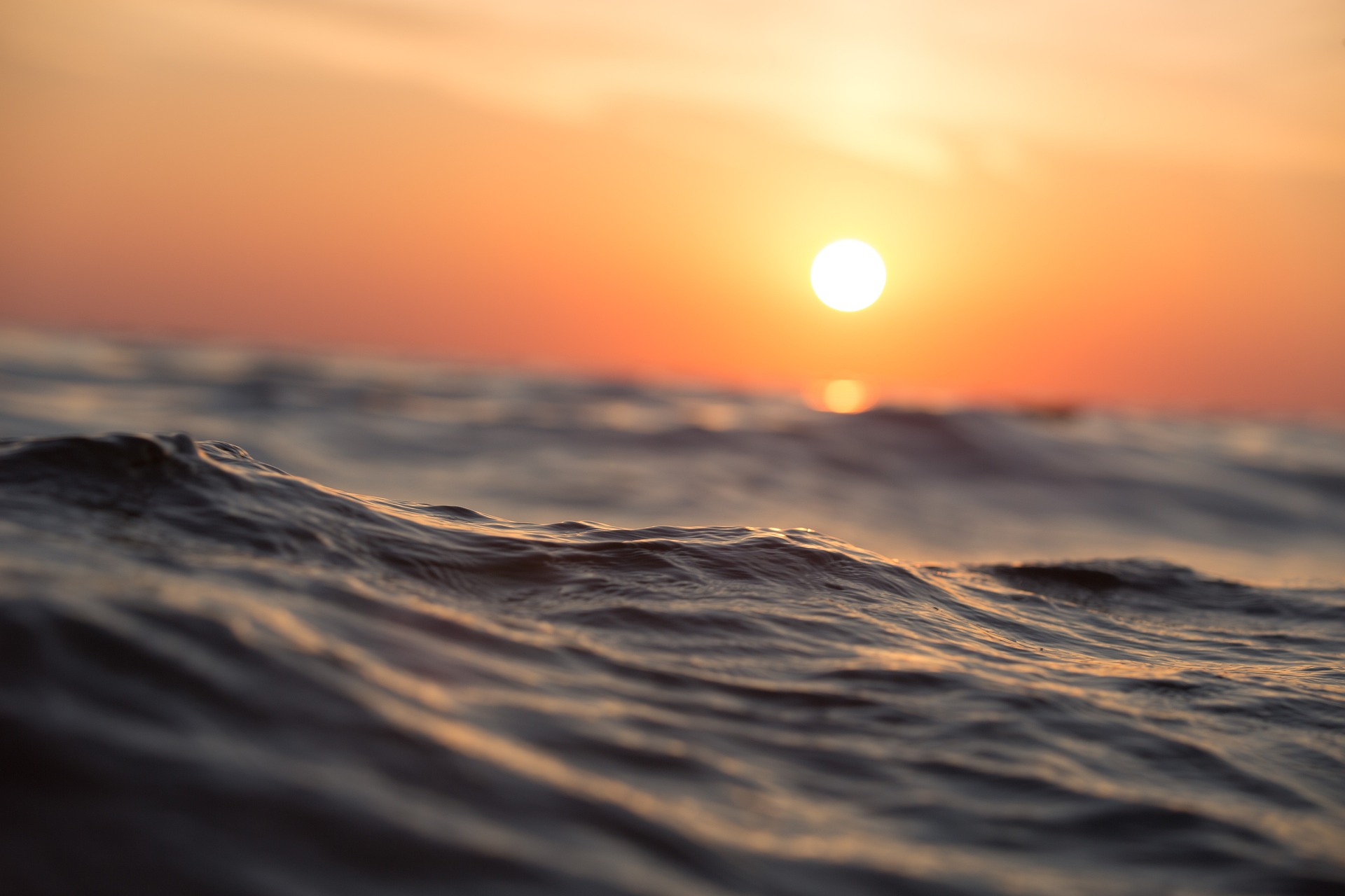 The ocean surface with the sun visible in low in the sky in the background