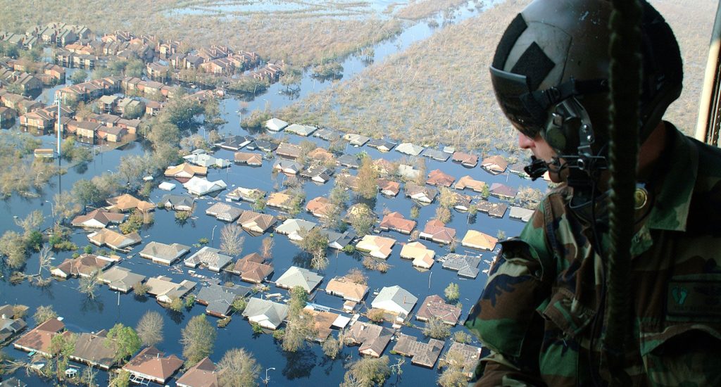 A soldier looking out of a helicopter over a flooded town