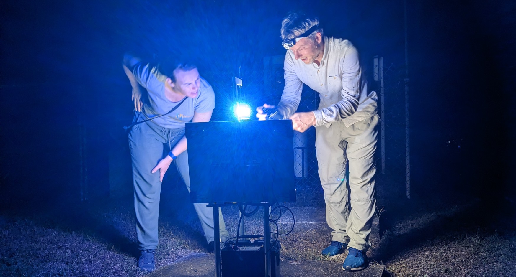 Two people with torches examining computer equipment at night