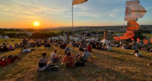Sunset at the Glastonbury Festival, showing people sitting on a hill looking over the festival