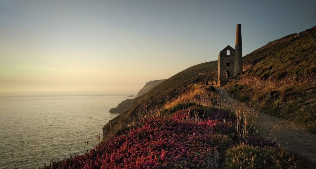 Remains of old industrial buildings, including a tall chimney, on a steep coastal slope