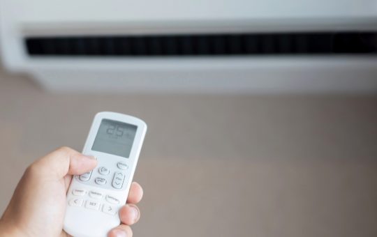 A hand holding the controller for an air conditioning unit