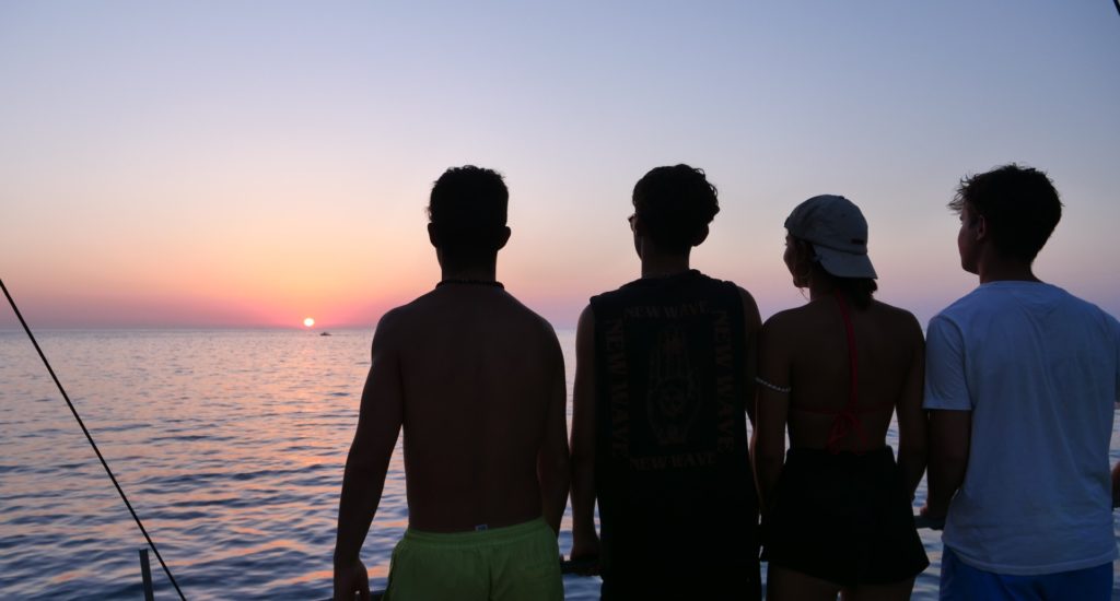 Four figures in silhouette, looking out over the sea at sunset