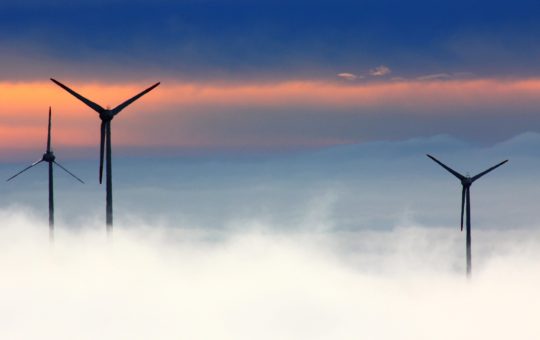 Wind turbines standing above low clouds or mist