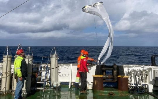 People in hard hats on a ship working with a large net used for research