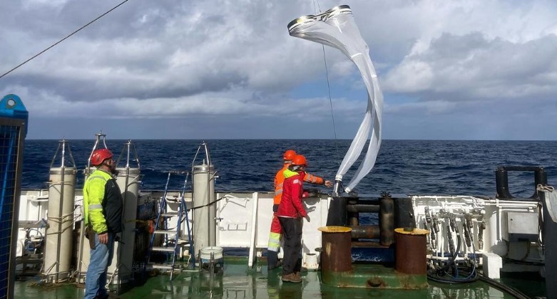 People in hard hats on a ship working with a large net used for research