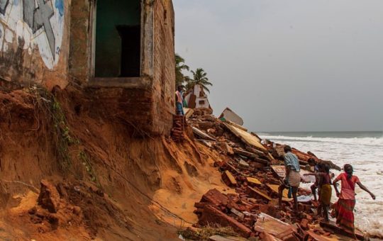 People walking by the ruins of buildings on the edge of an eroded section of coast at Bommiarpalayam along the Bay of Bengal coastline, in India.