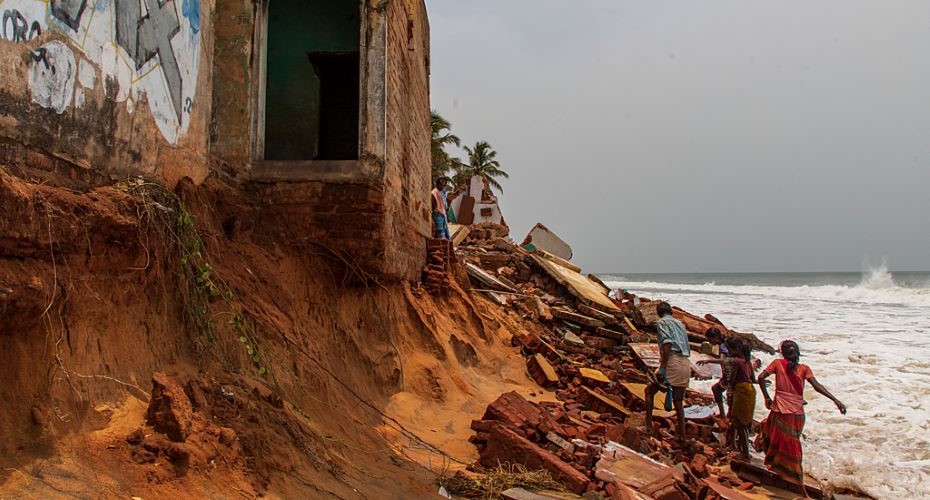 People walking by the ruins of buildings on the edge of an eroded section of coast at Bommiarpalayam along the Bay of Bengal coastline, in India.