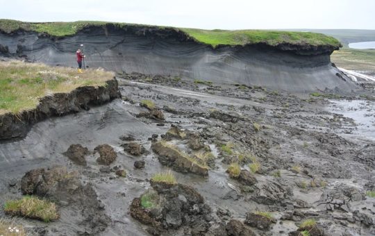 A person standing in a partially subsided landscape of mud (melted permafrost)