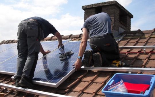 Two workers on a roof fixing solar panels