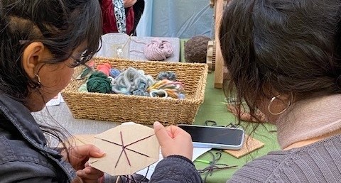 Two people at a table, working with some thread as they learn how to mend clothes