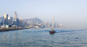 A small boat seen crossing Victoria Harbour, Hong Kong, with the city skyline visible in the background