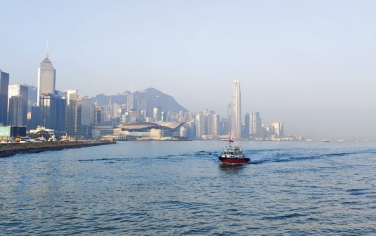 A small boat seen crossing Victoria Harbour, Hong Kong, with the city skyline visible in the background