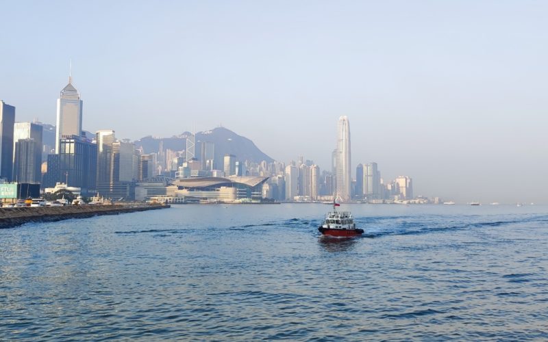 A small boat seen crossing Victoria Harbour, Hong Kong, with the city skyline visible in the background