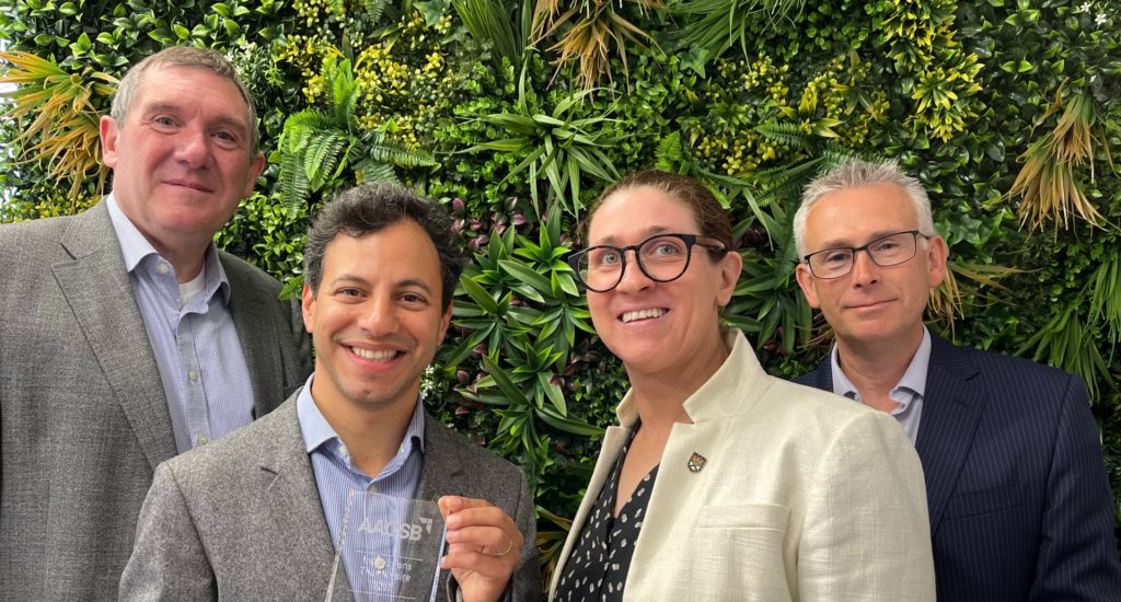 Four people standing with the AASCB award - a rectangular glass trophy