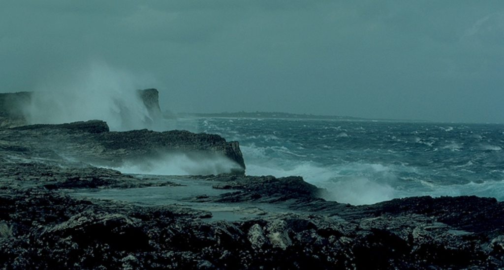 A rocky section of coastline with waves breaking under grey skies