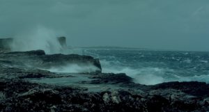 A rocky section of coastline with waves breaking under grey skies
