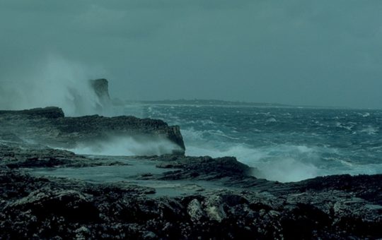 A rocky section of coastline with waves breaking under grey skies