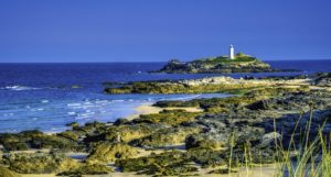 A lighthouse seen from the shore, with rocks and waves in the foreground