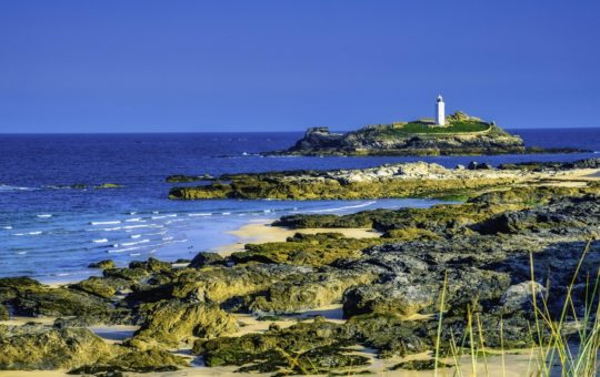 A lighthouse seen from the shore, with rocks and waves in the foreground