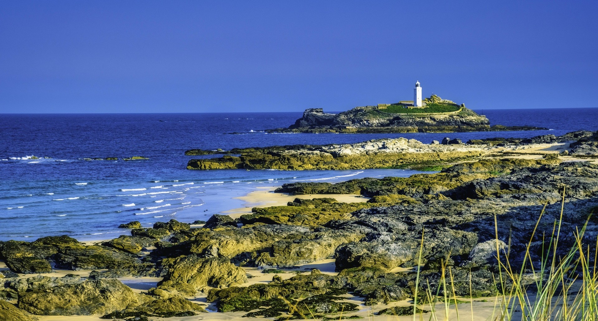 A lighthouse seen from the shore, with rocks and waves in the foreground