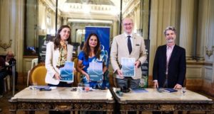 Gabriella Seiler, Malini Mehra, Stuart Brocklehurst, Carlos Milani standing behind a table in a large a grand room, holding copies of the climate guide