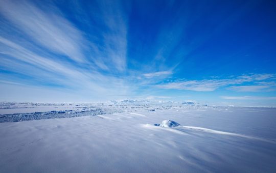 An icy landscape in Antarctica under blue skies with thin streaks of cloud