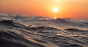 The sun seen low over a closeup shot of ripples on the ocean surface