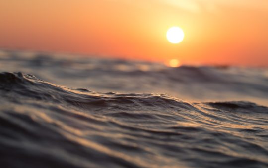 The sun seen low over a closeup shot of ripples on the ocean surface