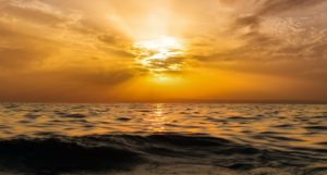 The sun setting in a partly cloudy sky over the ocean