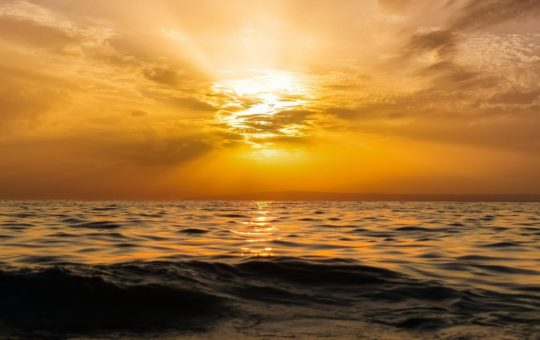 The sun setting in a partly cloudy sky over the ocean