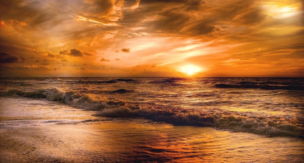 An image of sunset at a beach, with small waves rolling in