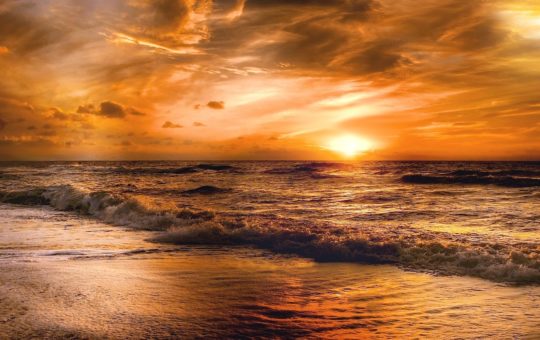 An image of sunset at a beach, with small waves rolling in