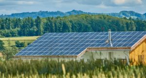 A wooden house in a field, with solar panels covering the entire roof