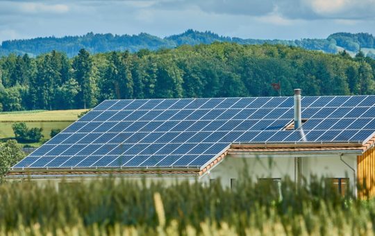 A wooden house in a field, with solar panels covering the entire roof