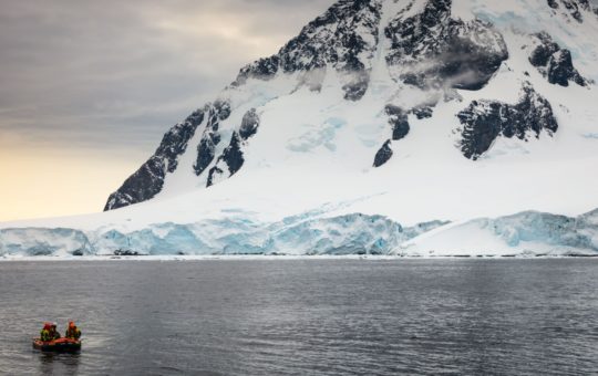 A small boat in the sea, with a snow-covered mountain visible in the background