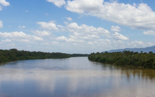 A wide stretch of river with forest on each side and blue sky and white clouds above