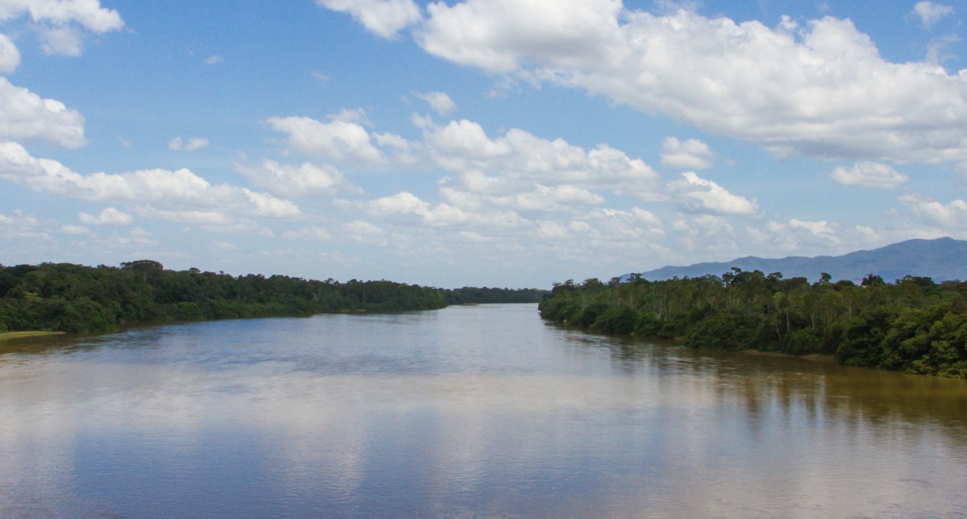 A wide stretch of river with forest on each side and blue sky and white clouds above