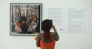 A person taking a photograph of a portrait on the wall.