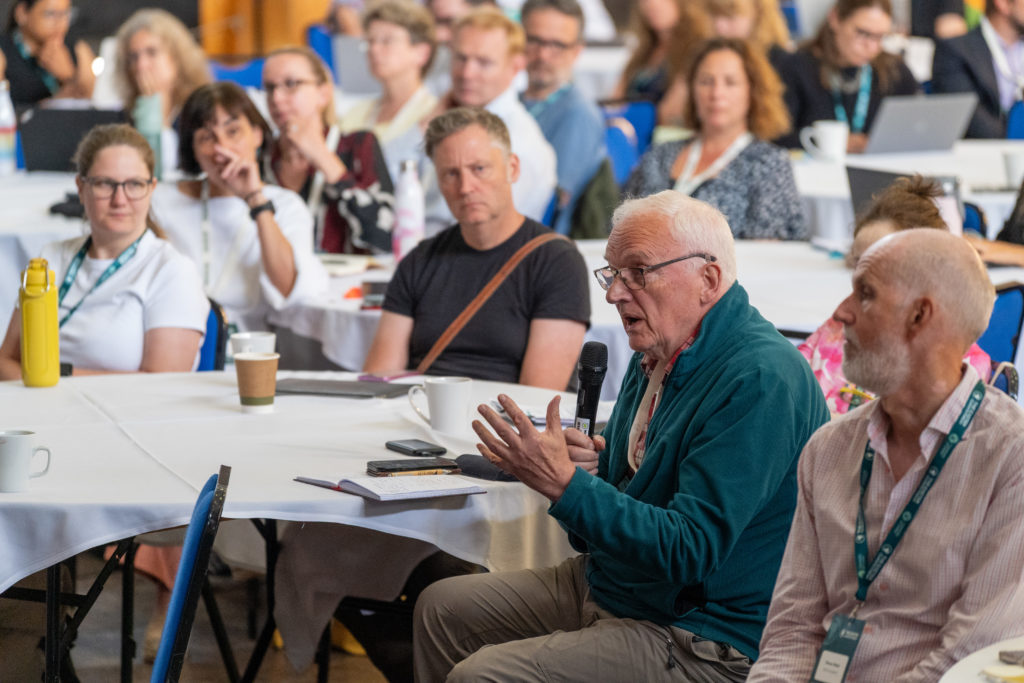 A man holding a microphone in the audience, asking a question at Exeter Climate Forum