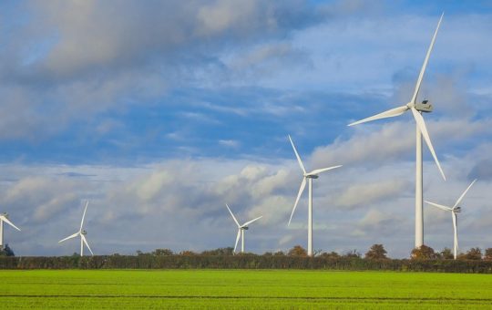 Wind turbines in green fields, with blue sky and clouds above