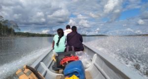 Three people sitting in the front of a boat on a river, pictured from behind