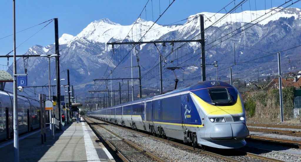 A Eurostar train in a station, with snow-capped mountains visible in the background