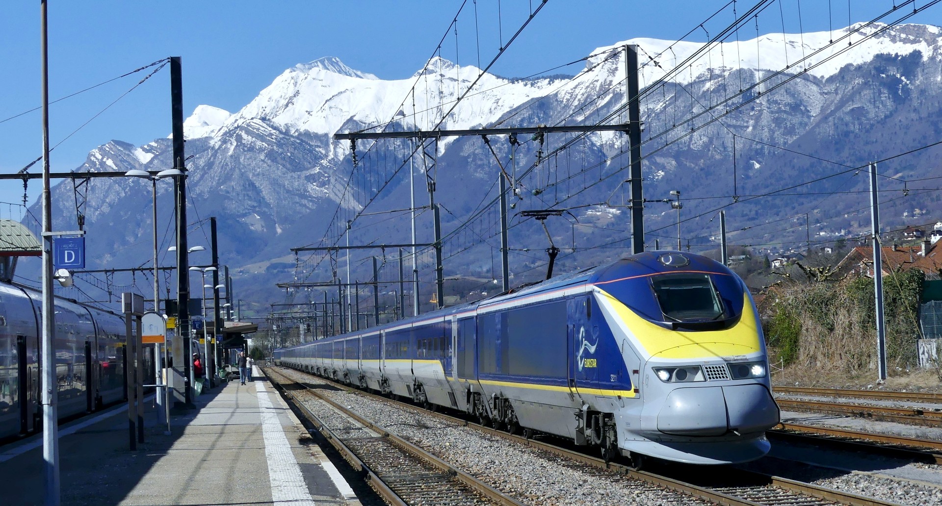 A Eurostar train in a station, with snow-capped mountains visible in the background