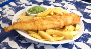 A plate of battered fish and chips with mushy peas